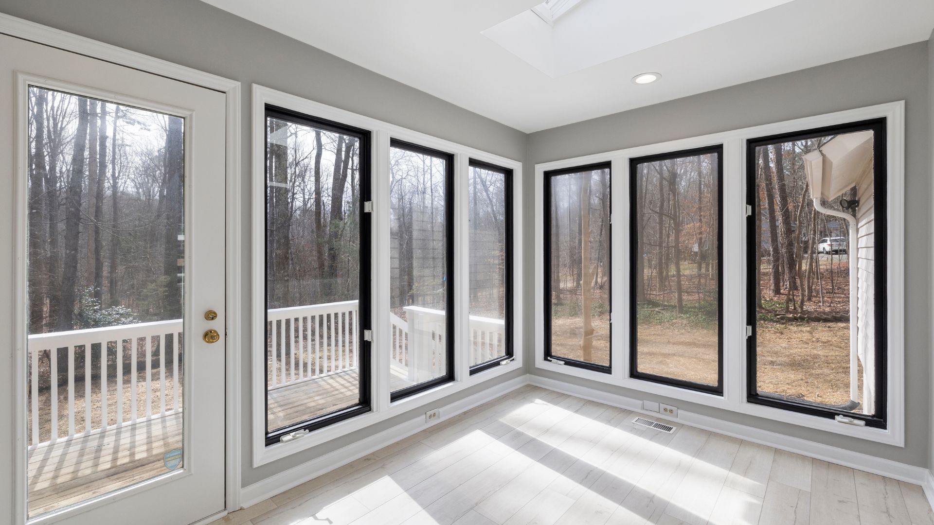 Bright sunroom with large windows overlooking bare winter trees and wooden deck