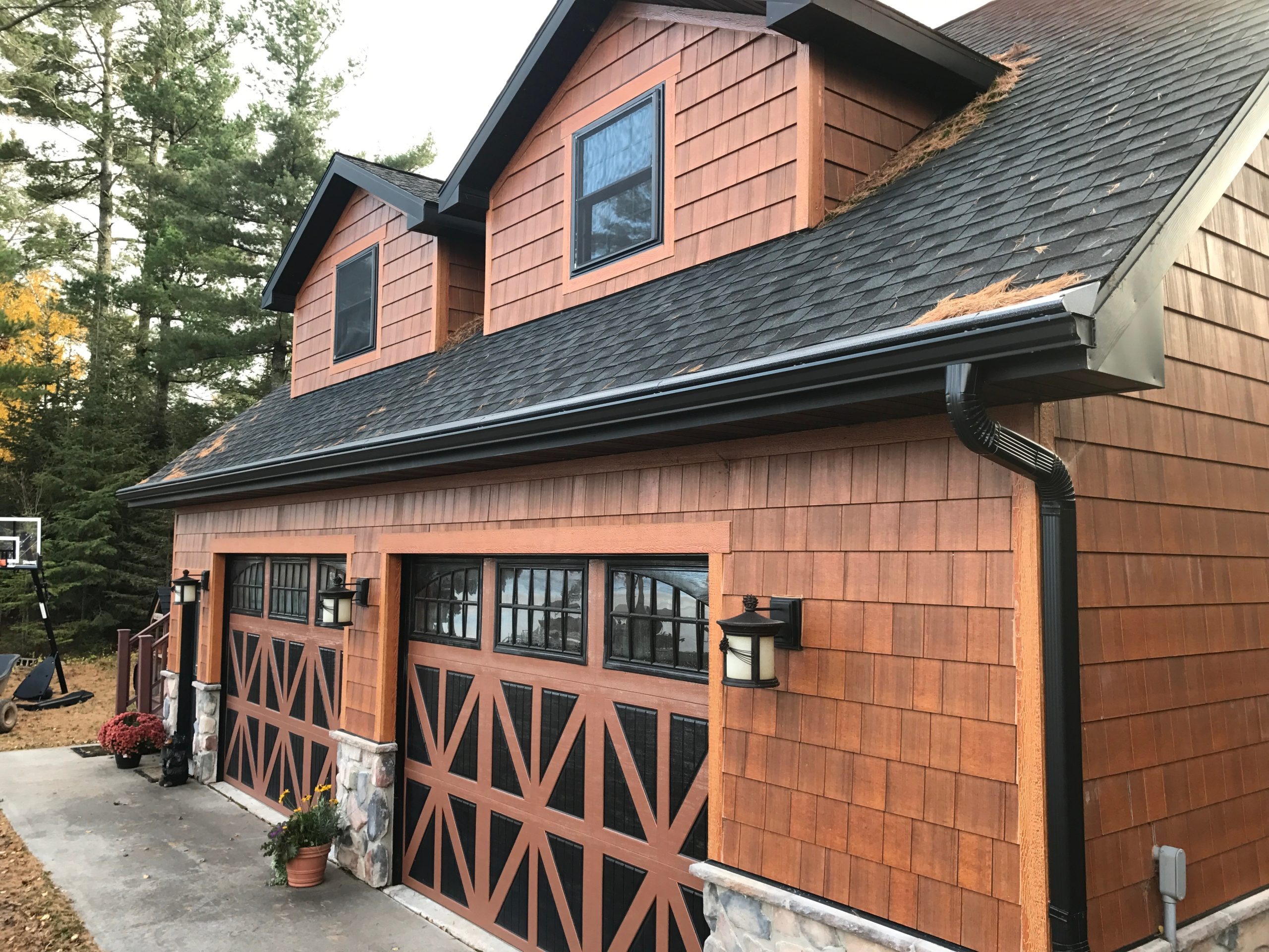 Cedar-sided house with decorative black garage doors and stone base