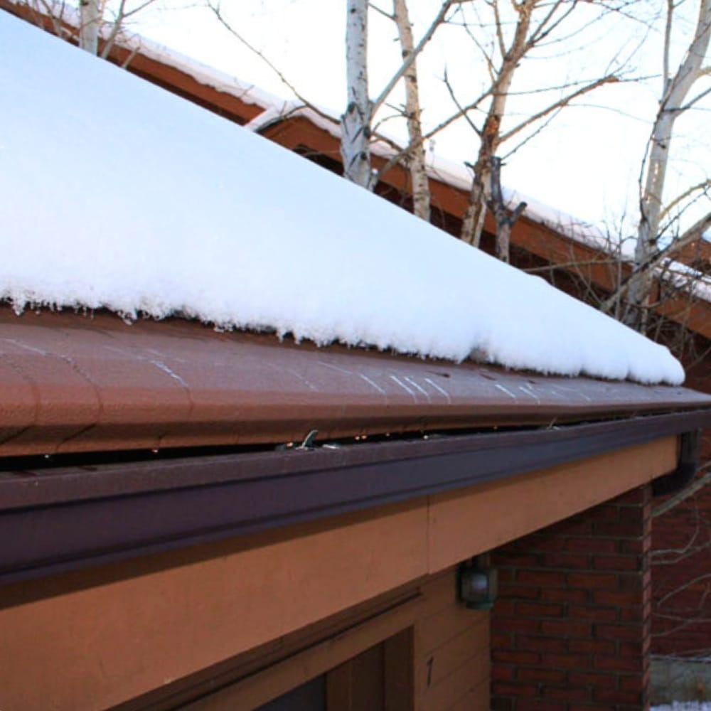 Snow-covered roof with icicles and bare birch trees in winter