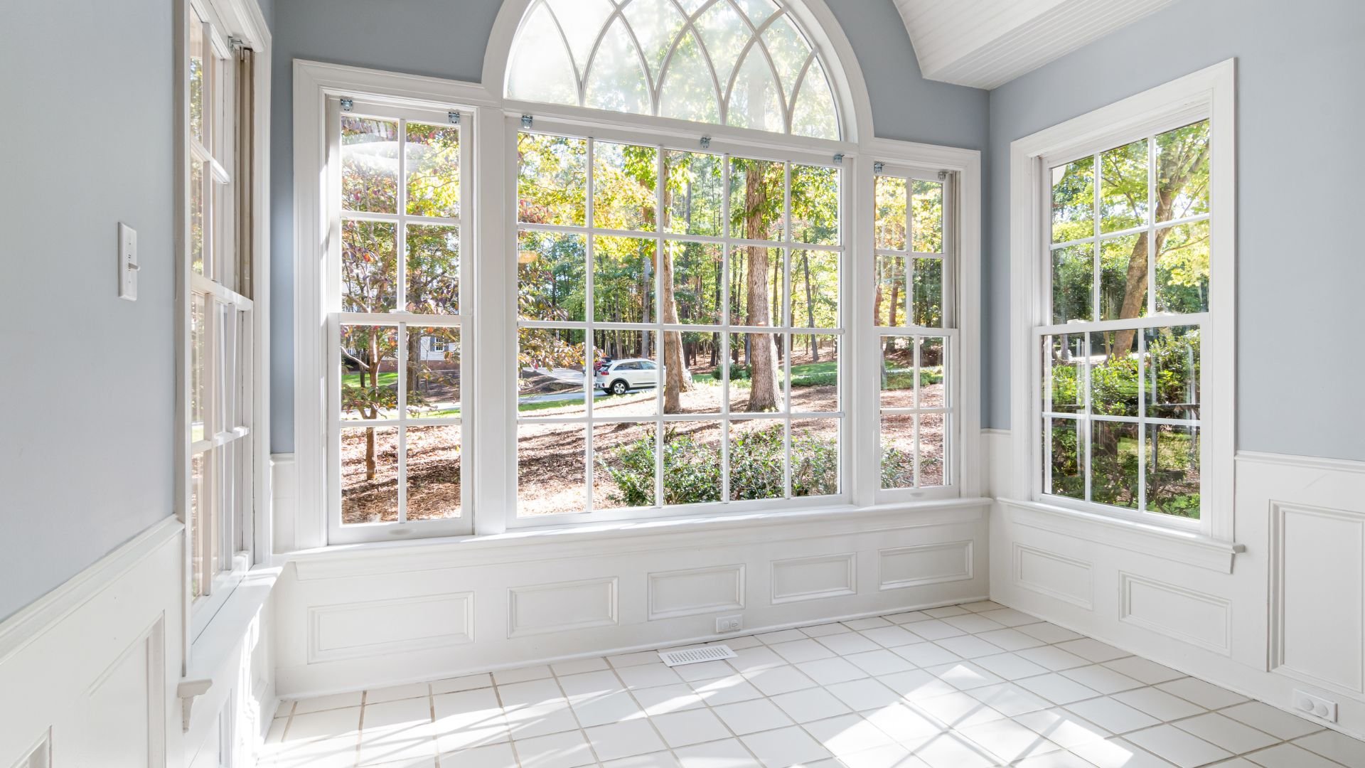 Bright sunroom with large white windows overlooking wooded forest landscape